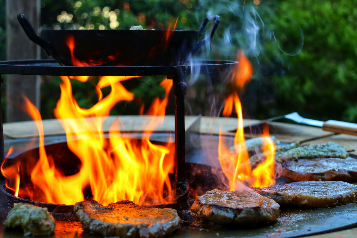 Steaks und Spieße brutzeln auf einem Grill mit orangefarbenen Flammen.