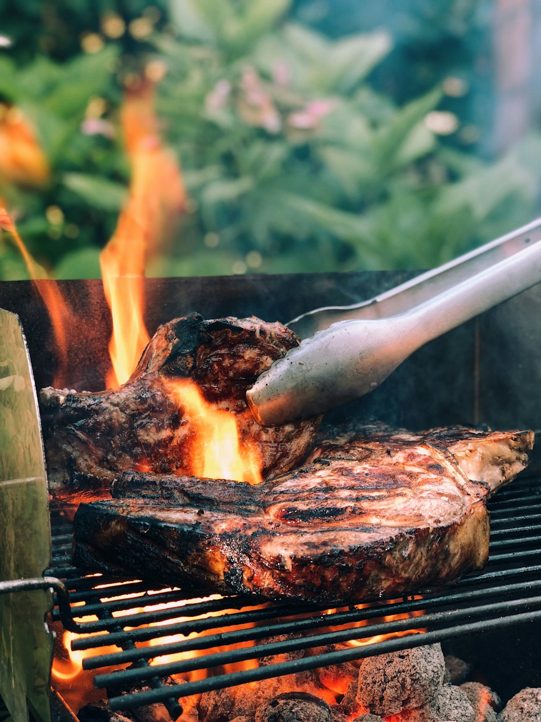 Steaks auf einem Grill über offenem Feuer mit einer Zange.