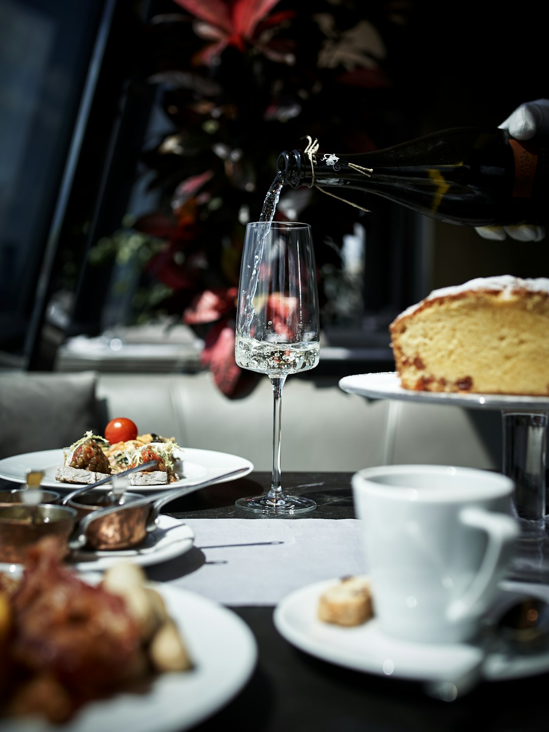 Behandschuhte Hand gießt Sekt in ein Sektglas neben Kuchen und Vorspeisen.